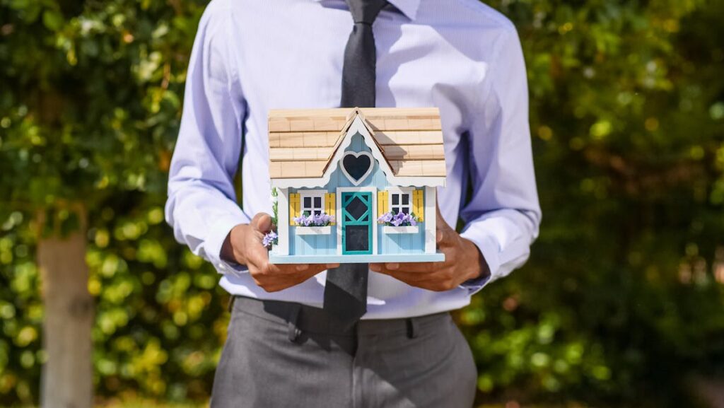 A person in business attire holding a colorful model house outdoors, reflecting the role of the National Association of Realtors in guiding homebuyers.